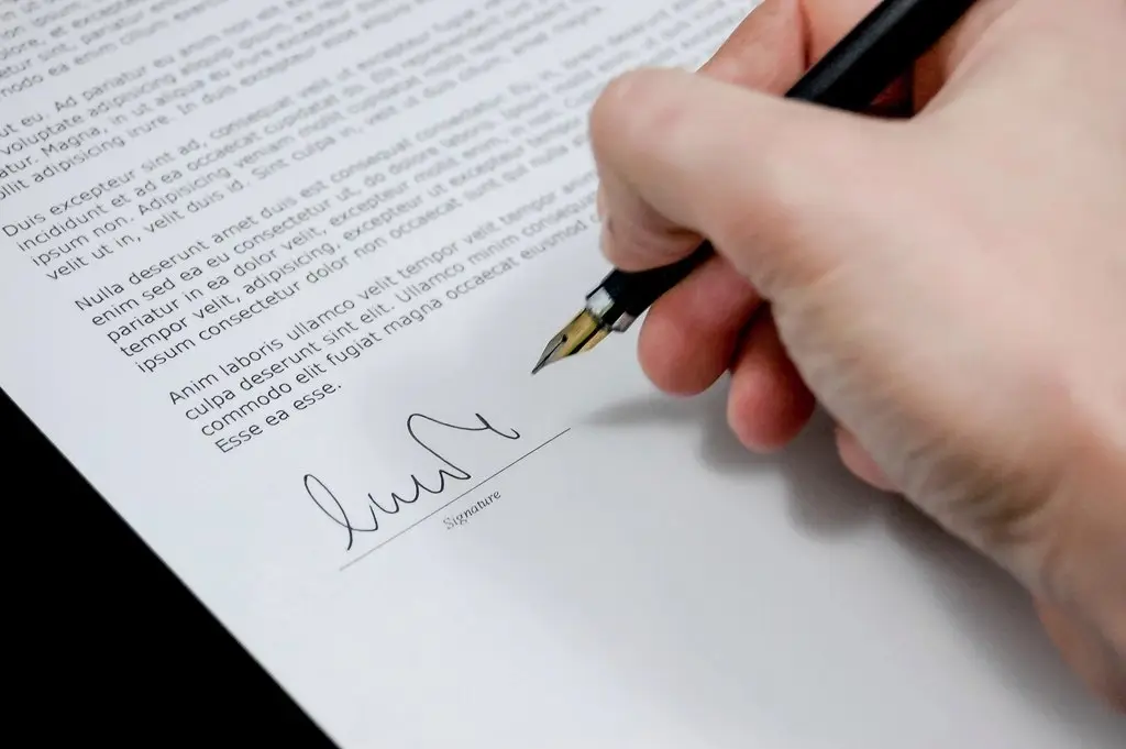 Hand signing a document with a pen, representing promoter funding agreements